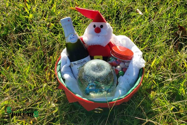 Christmas gift basket on the grass with a Santa plush, sparkling apple cider, candy jar and snow globe