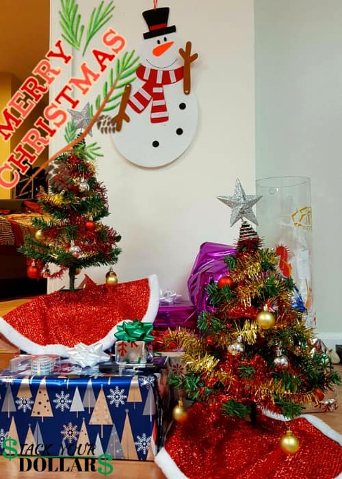 Two tiny Christmas trees on top of presents with Snowman wall hanging