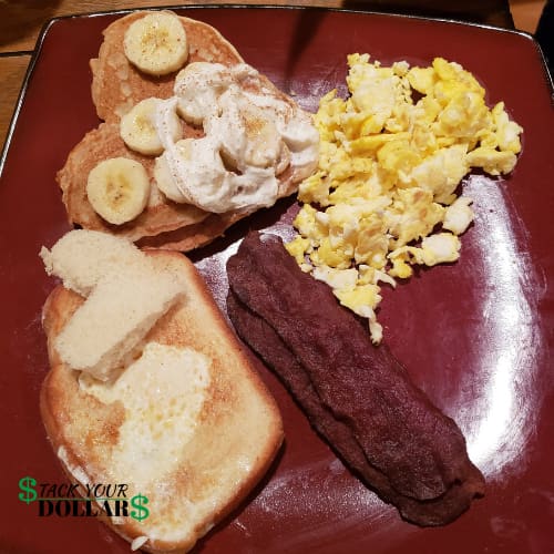 Valentine's day breakfast with heart-shaped pancakes and bananas, scrambled eggs, bacon, and toast with a cut-out heart filled with egg.